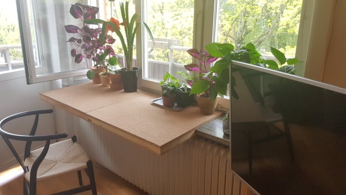Hemmagjord skrivbordsyta i trä ovanpå radiator med växter och stol.