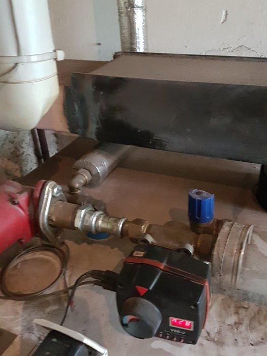 En rad med olika röranslutningar och en elektronisk pump eller ventil monterad på en vägg i ett byggprojekt.