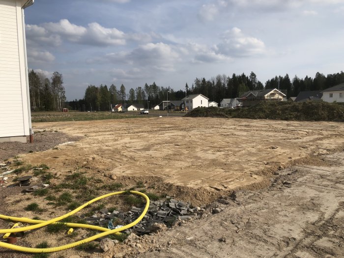 Avschaktad tomt med jämn mark vid husbygge, grushög och gul slang synlig.