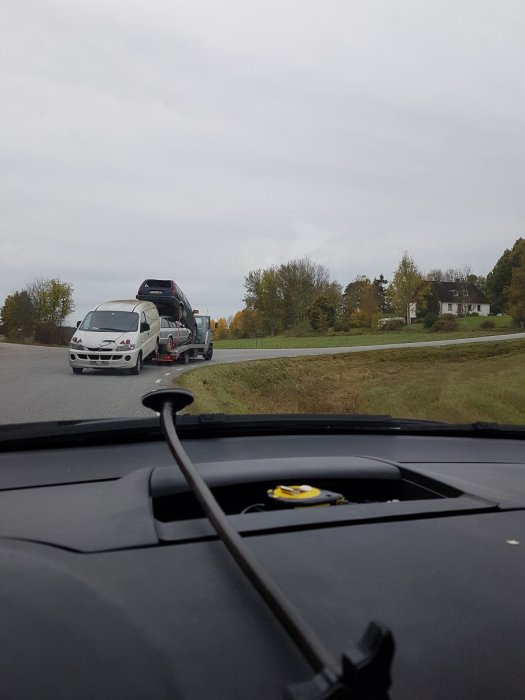 Biltransport med en bil på taket av en annan på släpvagn sedd från en annan bil.