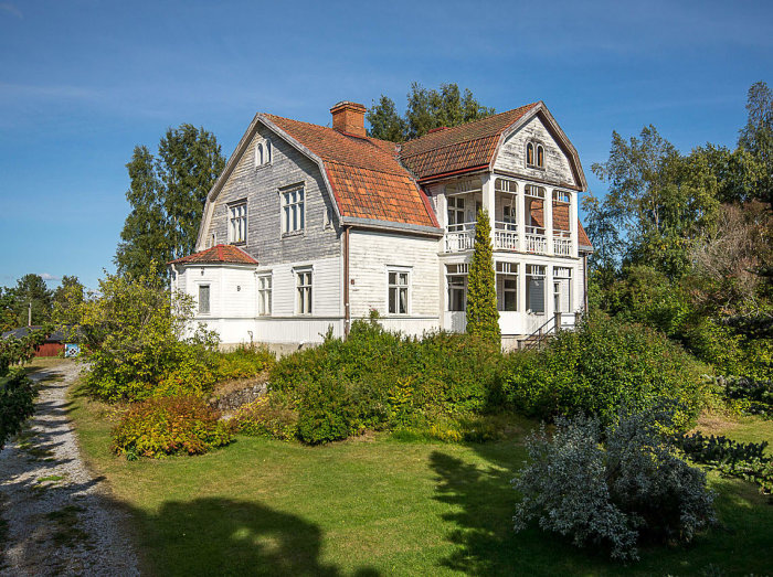 En vit, klassisk villa från 1916 omgärdad av grönska med en flygelbyggnad, till salu för 650 000 kr.