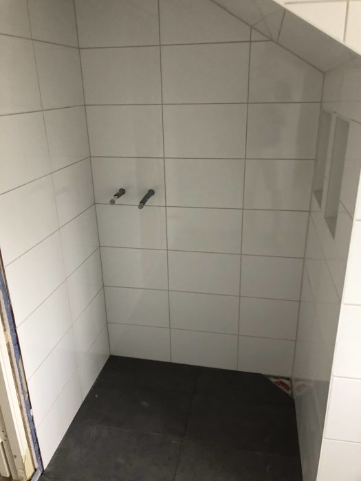 Nyinstallerade vita kakelväggar och grått kakelgolv i ett ofogat badrum under renovering.