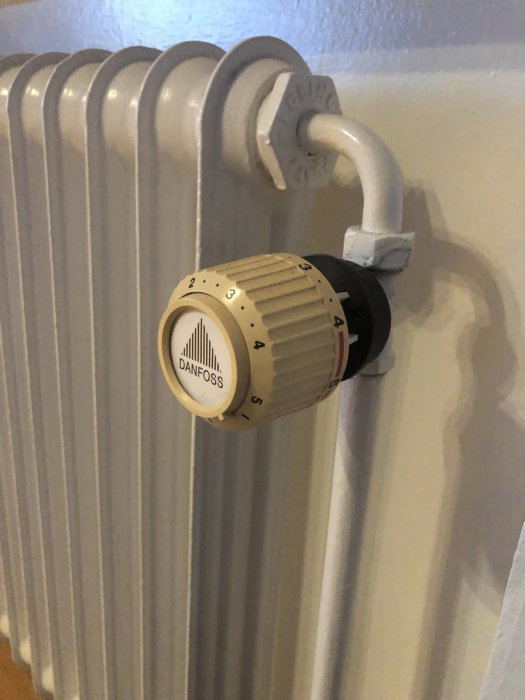 Gammal radiator med en vit Danfoss termostat och anslutning mot väggen.