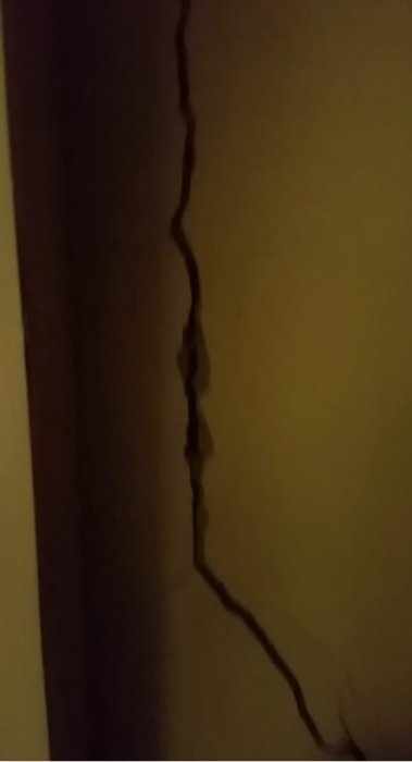Lång sammanhängande spricka i vägg i ett äldre betonghus, potentiell sättningsskada.