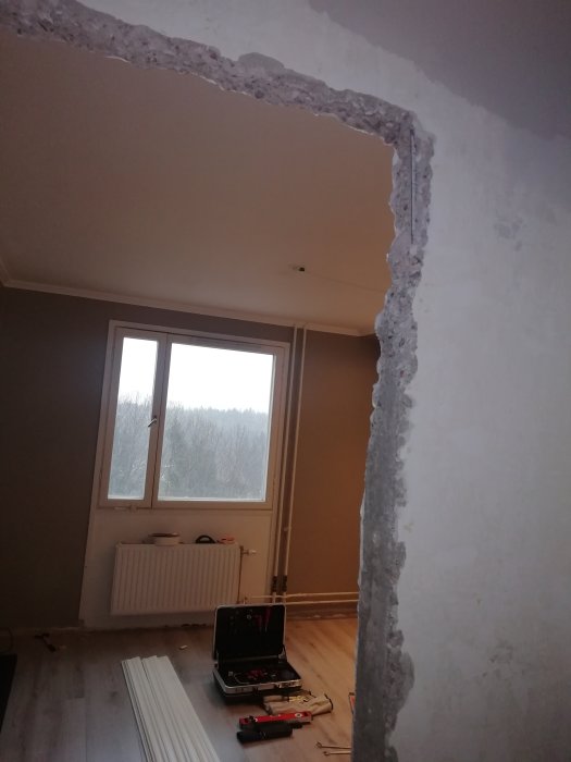 Renoveringsprojekt med avlägsnad dörrkarm som avslöjar grov betong och armering i en väggöppning, verktyg på golvet.