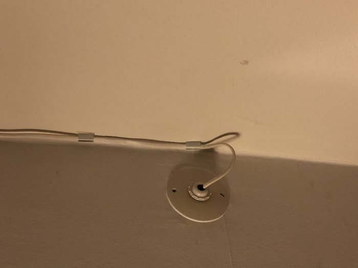 Elkabel löper längs väggen till ett oanvänt vägguttag i ett vardagsrum.