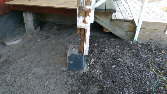 Hörnstolpe på veranda vilar på en liten träkloss med rivet däck i bakgrunden.