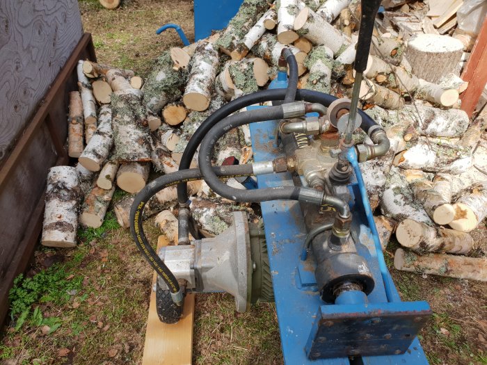 Hydraulik på en vedkap bland staplade björkvedsträn.