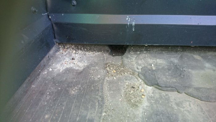 Äldre takpapp på balkonggolv med synliga sprickor och skador nära en svart balkongräcke och slitage runt ett avloppshål.
