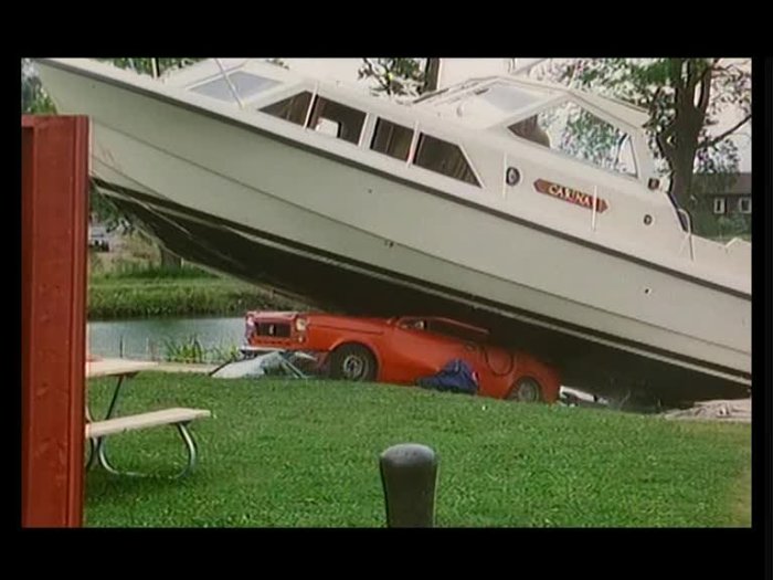 Båt ovanpå krossad röd bil vid en kaj som föreslår felaktig lastning eller olycka.