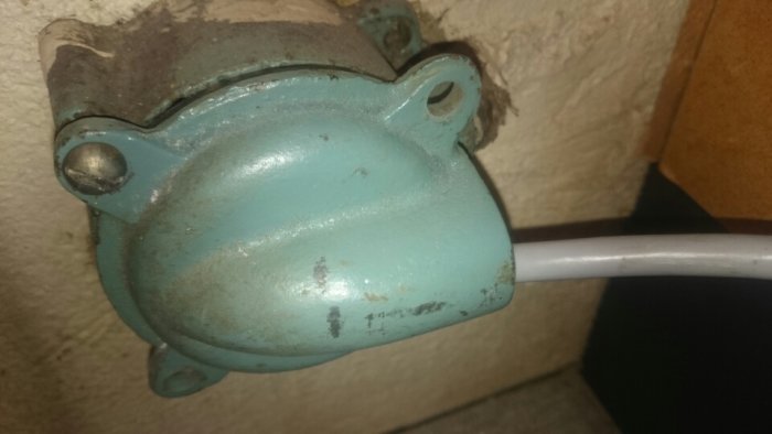 Närbild av en installerad blå eldosa med en vit kabel som sticker ut, fästad mot en vägg.