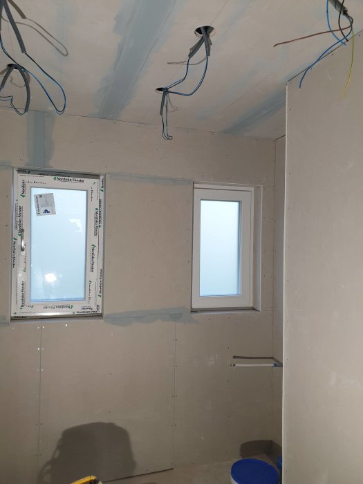 Ett badrum under renovering med väggar förberedda för kakel, utstickande elkablar och tre fönster.