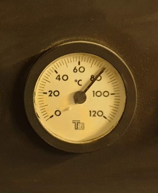 En termometer som visar cirka 80 grader Celsius, monterad på en yta i en pannrumsmiljö.
