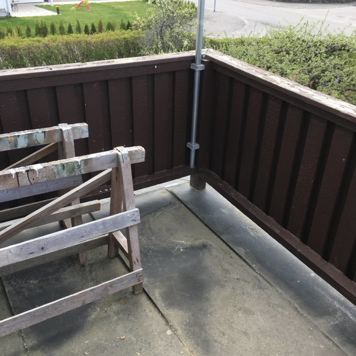 Hörn av en balkong på andra våningen med bruna staket, betonggolv och en gammal trästege, redo för trallprojekt.