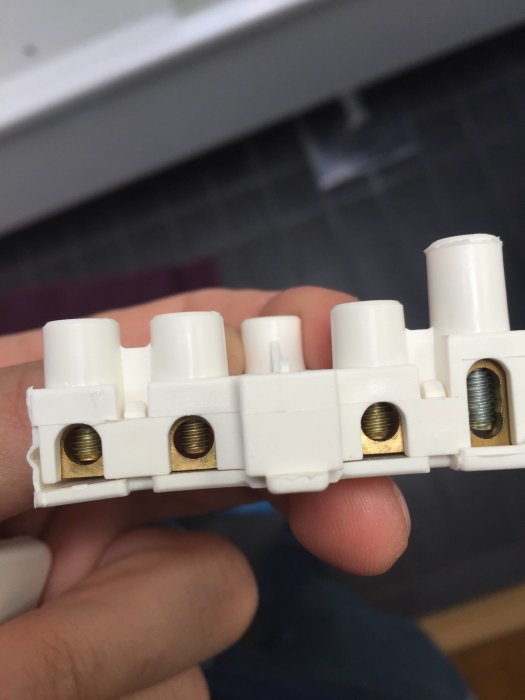 Hand håller en vit kopplingsdosa med synliga skruvanslutningar för elektrisk installation.