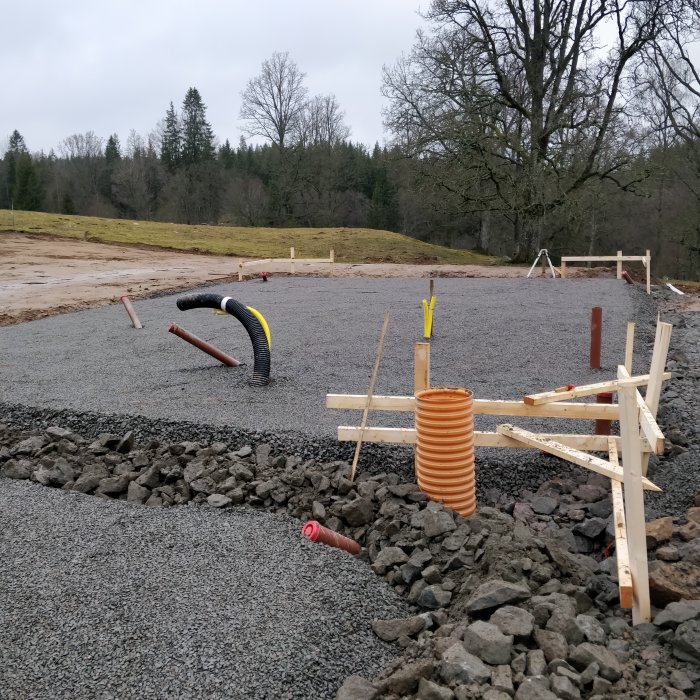 Gjuten betongplatta för husbygge med rör och utsatta gränspinnar på en byggarbetsplats.