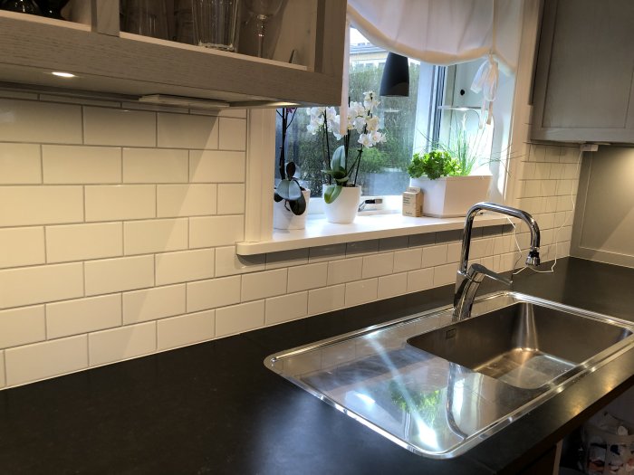 Nyinstallerat vitt kakel över köksbänken med öppet fönster och diskho.