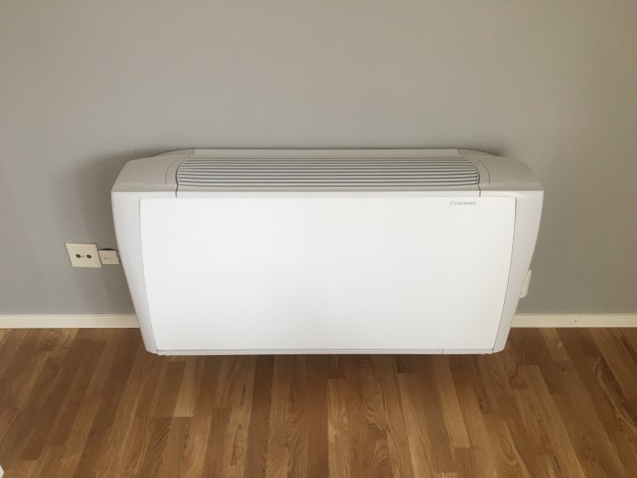 Sabiana-fläktkonvektor installerad vid vägg ovanför parkettgolv i ett rum.