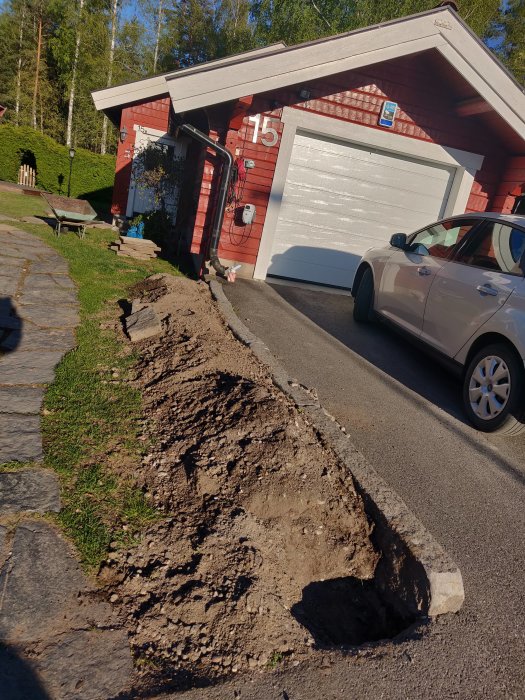 Uppgrävd jordbädd längs garage med synligt berg vid kanten redo för plantering och kantstensinstallation.