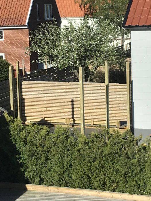 Påbörjat byggprojekt av hög pergola utan tak med synliga trästolpar och plankvägg mot bakgrund av hus.