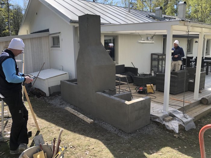 En person murar en utomhuskamin på en bakgård med hus och altan i bakgrunden.