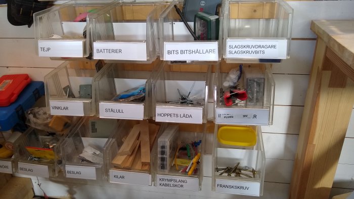 Organiserade genomskinliga förvaringslådor med etiketter, fyllda med byggmaterial och verktyg.