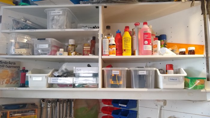 Välorganiserade hyllor i verkstad med märkta förvaringslådor och flaskor för skruvar och förbrukningsmaterial.