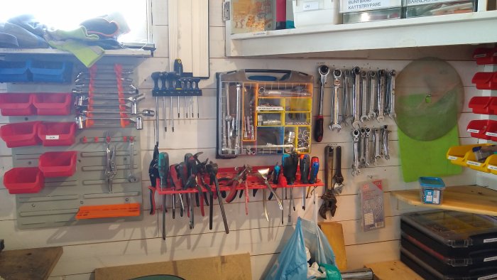 Verktygsvägg i verkstad med organiserade handverktyg, skiftnycklar och skruvar i sortimentlådor.