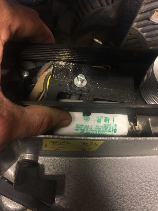 Hand som håller en Ecofill MLR25-kondensator inuti en maskin, smuts och sladdar synliga.