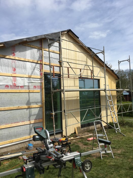 Halvfärdig fasad på hus med ställning och snickeriverktyg i förgrunden.