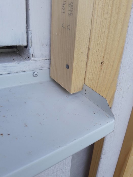 Detaljbild av fönster där träsnitt för listning övats på och är delvis installerad vid vitmålat fönsterbräde.