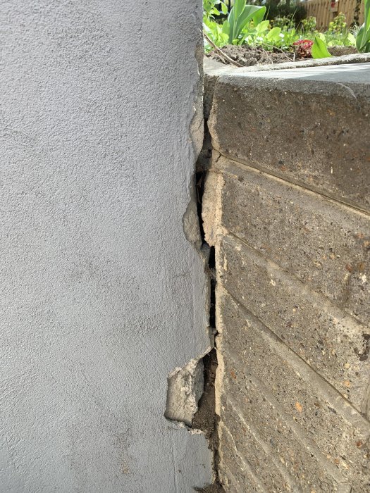 Skada där garagevägg möter stenvägg med synlig spricka och erosion som behöver reparation.