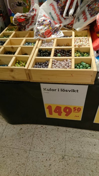 Trähyllor med olika färgade spelkulor i lösvikt, pris 149,50 SEK/st, med butikens golv synligt.