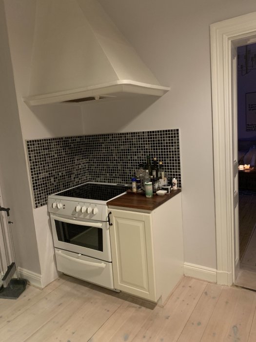 Kökshörn med mosaikkakel ovanför bänkskiva och vit spis, redo för renovering.