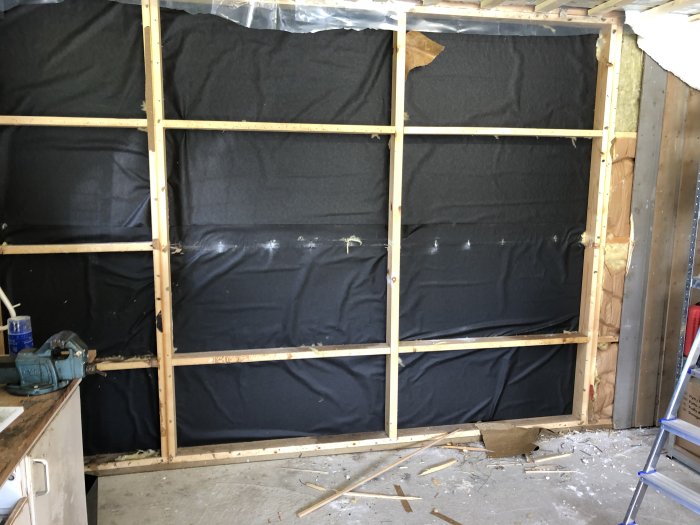 Rivningsfas i garage med exponerat regelverk och svart byggplast, spillror på golvet.