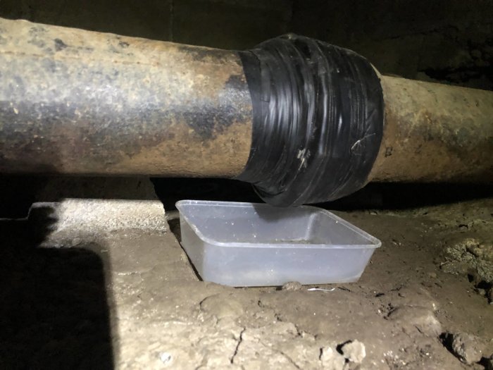 Vulktejp applicerad på rörskarv ovanför en plastbehållare på ett grusigt underlag.