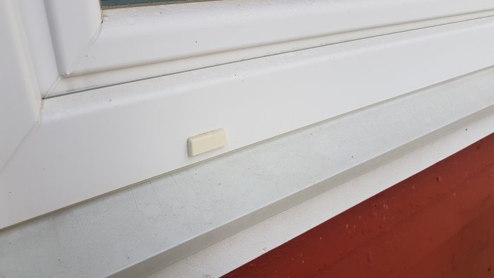 Del av ett fönster med ett saknat plastskydd på fönsterbrädan och spår av smuts under fönstret.