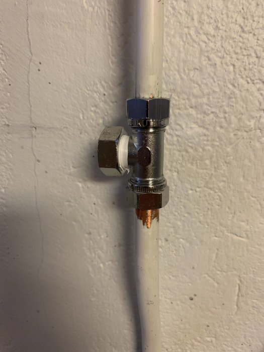 Plomberad ballofixventil på vit vattenledning mot grå vägg med synliga rörkopplingar.