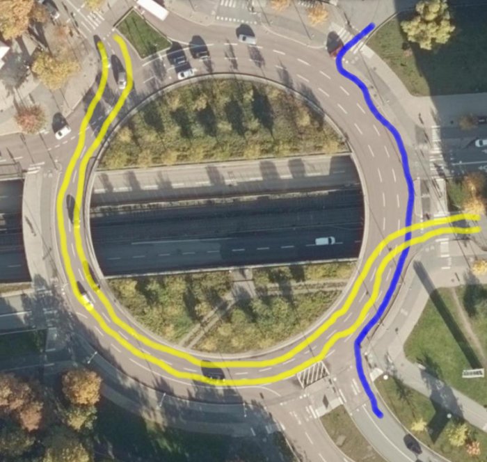 Flygbild av en rondell med markerade rutter i blått och gult som illustrerar olika körfält och trafikflöden.