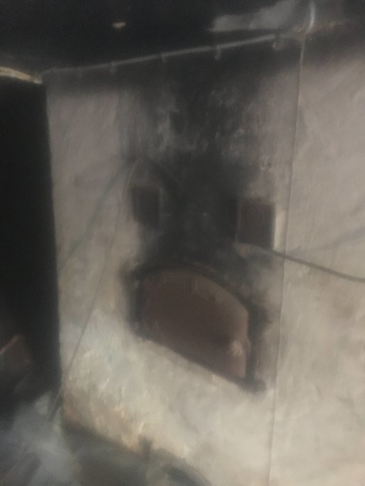 Otydlig bild av en stenmur med en gammal bakugn i en källare från 1875 med synliga bjälkar i taket.