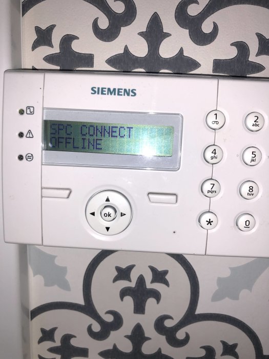 Siemens SPC Connect larmsystem display visar meddelandet "OFFLINE" på en vägg med dekorativ tapet.