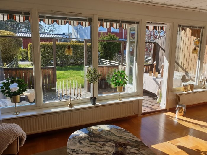 Inredning med trägolv, fönster med utsikt över trädgård och solbelyst altan.