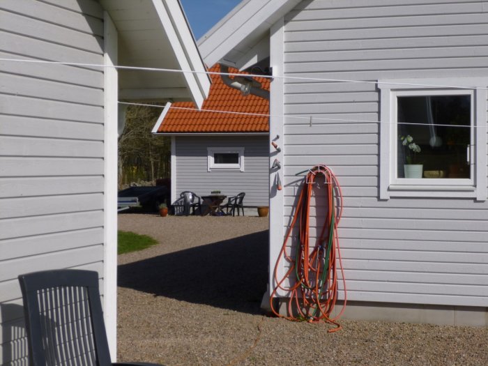 Husfasad målad med ljus färg betecknad Morgondis och ett mindre hus i mörkare nyans i bakgrunden, med en trädgårdsslang hängande på väggen.