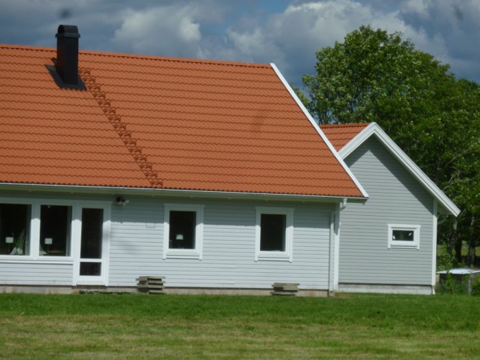 Renoverat boningshus målat i ljus färg "Morgondis" och småhus i mörkare nyans "S2500-N" under soligt väder.