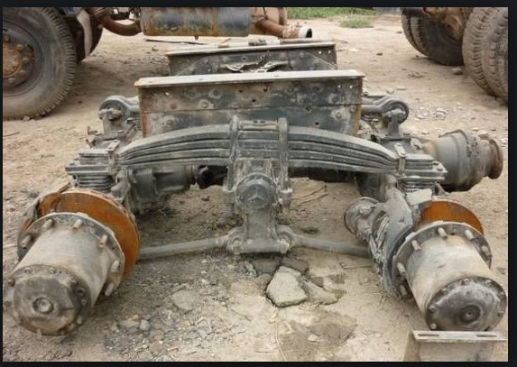 Demonterad lastbilsboggie med två axlar och fjädringssystem synlig på marken.