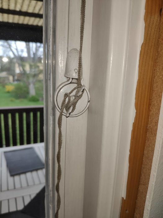 Ett gammalt vred för persienn på ett fönster med synlig snöre och utsikt mot en veranda.