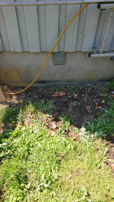 Yttervägg till hus med ventilation i grunden och en gul sladd, potentiell plats för ny krypgrundsöppning.