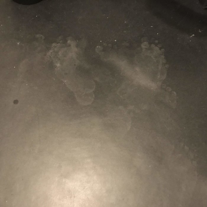 Fotavtryck på ett svart golv som visar smuts och fotspår.