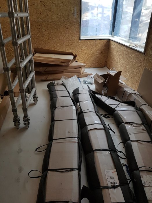 Ett trapphus under renovering med en ställning, OSB-skivor på väggarna och oöppnade förpackningar med obehandlade furutrappor.