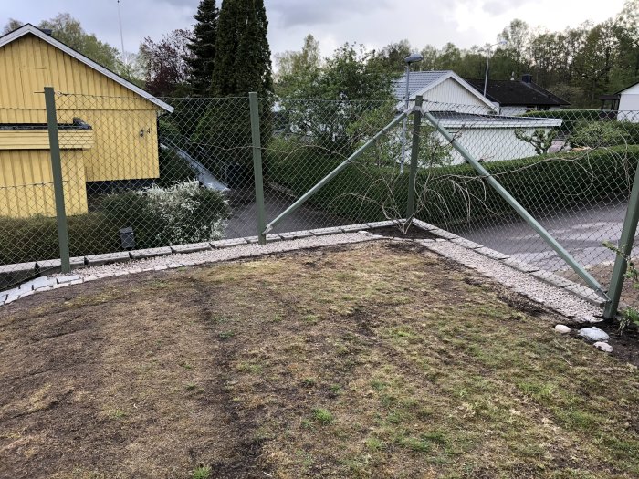 Pågående arbete med komposit-trall och ny kantsten längs trädgård med gult hus och staket.